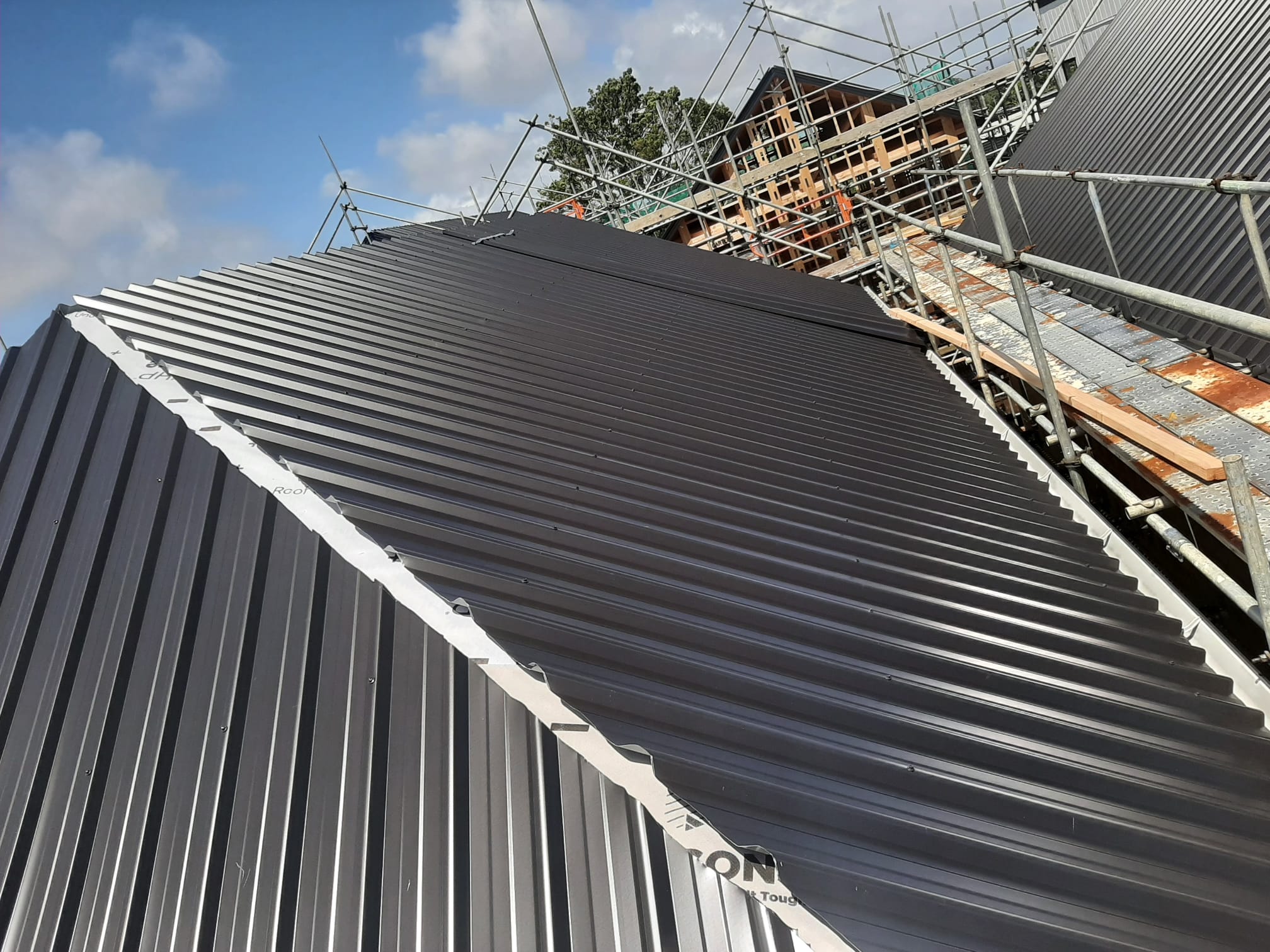 Wide view of Coloursteel longrun roof partway through install â€” Auckland new build
